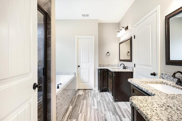 bathroom featuring visible vents, two vanities, a sink, and a bath