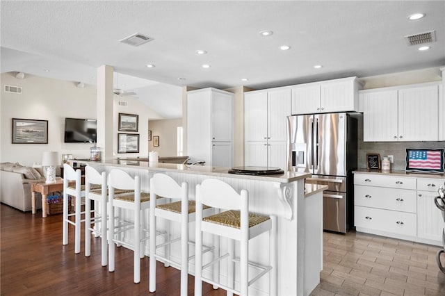 kitchen featuring a kitchen breakfast bar, open floor plan, visible vents, and stainless steel refrigerator with ice dispenser