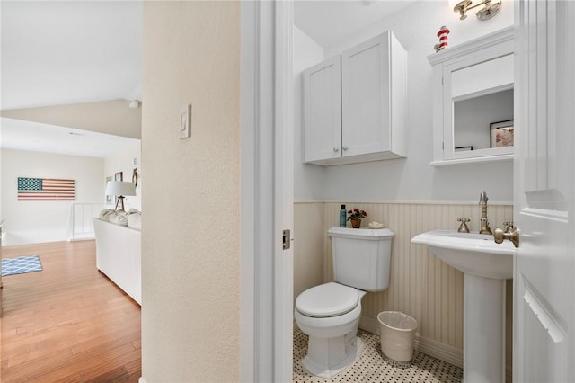 bathroom with vaulted ceiling, toilet, wood finished floors, and wainscoting