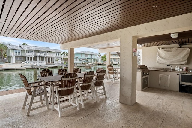 view of patio / terrace featuring a water view, area for grilling, a residential view, outdoor dining area, and an outdoor kitchen