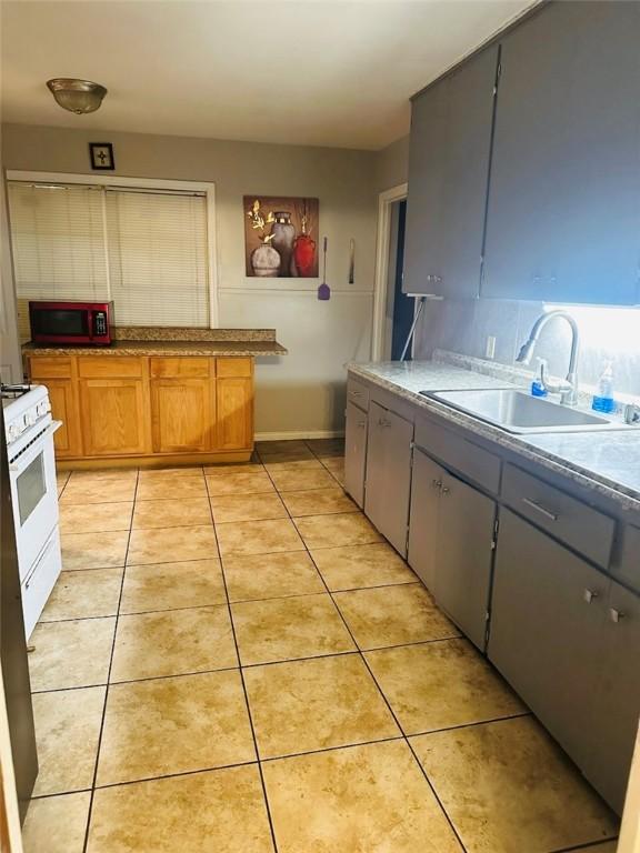 kitchen featuring decorative backsplash, white gas range oven, gray cabinetry, sink, and light tile patterned floors