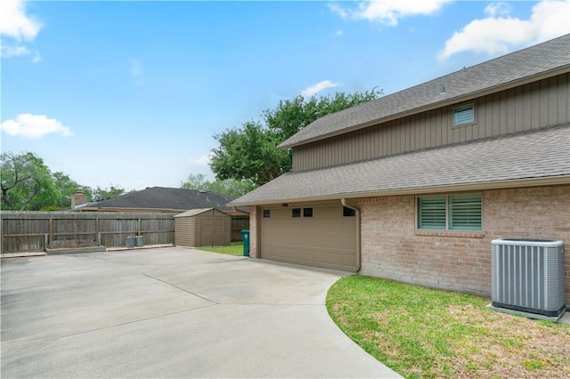 view of side of property with central AC, brick siding, a shingled roof, and a storage shed