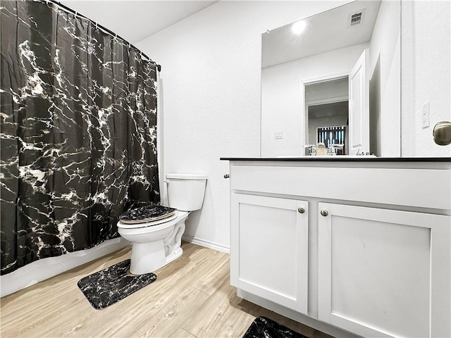 bathroom with wood-type flooring, vanity, toilet, and curtained shower