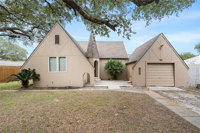 tudor house featuring a garage, driveway, a shingled roof, fence, and stucco siding