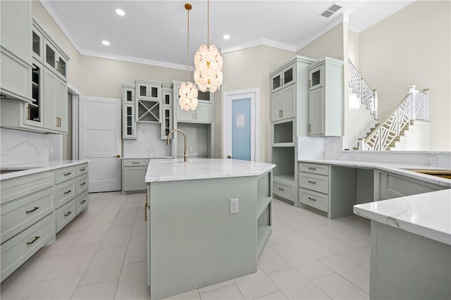 kitchen featuring a center island with sink, visible vents, ornamental molding, decorative backsplash, and a sink