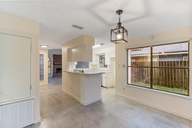 kitchen with sink, hanging light fixtures, a textured ceiling, a brick fireplace, and kitchen peninsula