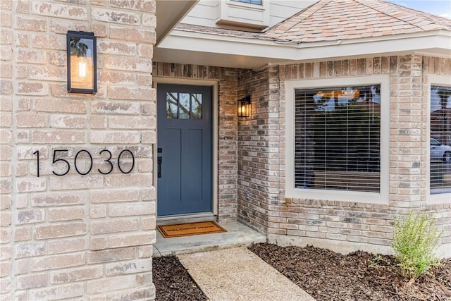 property entrance featuring brick siding and roof with shingles