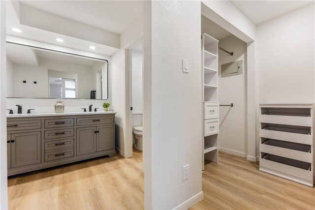 full bath with toilet, a sink, wood finished floors, double vanity, and a walk in closet