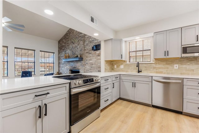 kitchen featuring tasteful backsplash, stainless steel appliances, light countertops, light wood-style floors, and a sink