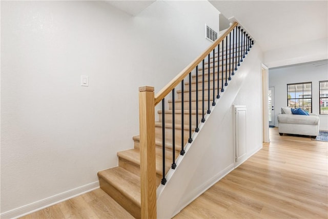 staircase with baseboards, visible vents, and wood finished floors