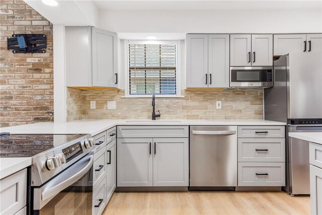 kitchen featuring a sink, light countertops, appliances with stainless steel finishes, light wood finished floors, and tasteful backsplash