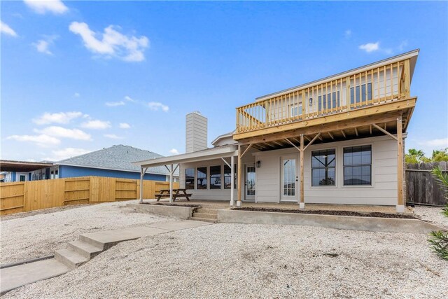 rear view of house featuring a deck, fence, a chimney, and a patio