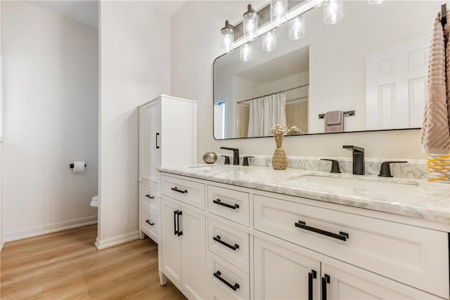 full bath with double vanity, a sink, baseboards, and wood finished floors