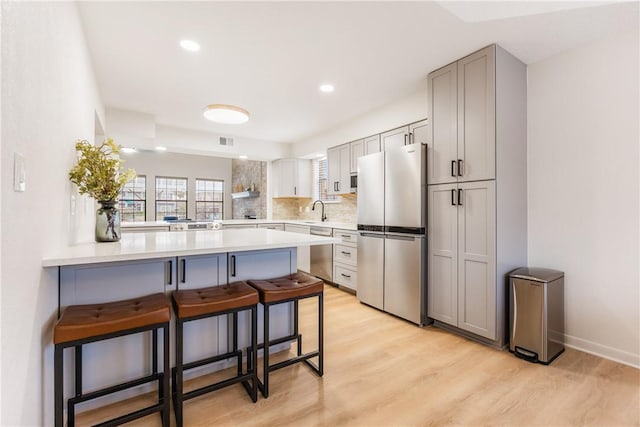 kitchen featuring appliances with stainless steel finishes, a breakfast bar area, a peninsula, light countertops, and a sink