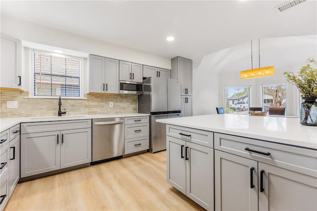 kitchen featuring stainless steel appliances, light countertops, a sink, and gray cabinetry