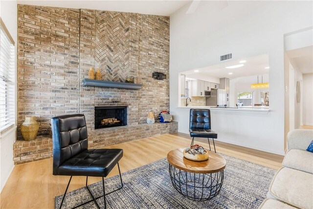 living area with visible vents, a fireplace, light wood-style flooring, and a towering ceiling