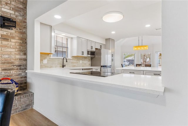 kitchen featuring a peninsula, tasteful backsplash, stainless steel appliances, and decorative light fixtures