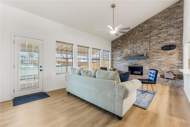 living room featuring ceiling fan, high vaulted ceiling, light wood-style flooring, baseboards, and a brick fireplace