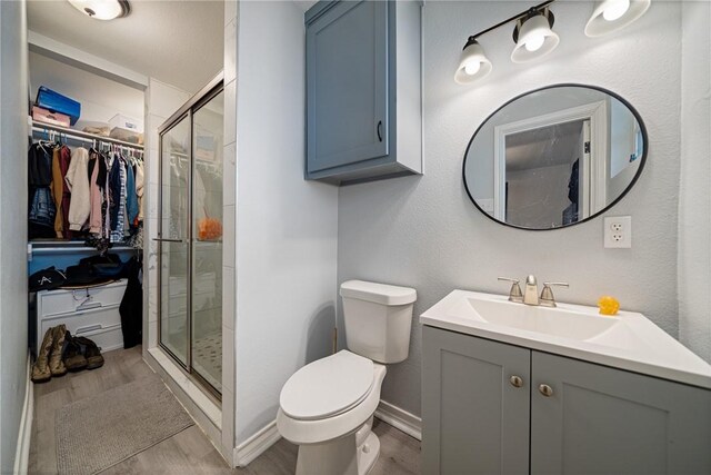 bathroom with hardwood / wood-style floors, walk in shower, vanity, and toilet