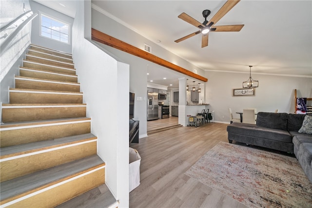 living area featuring visible vents, stairs, crown molding, light wood-type flooring, and ceiling fan with notable chandelier