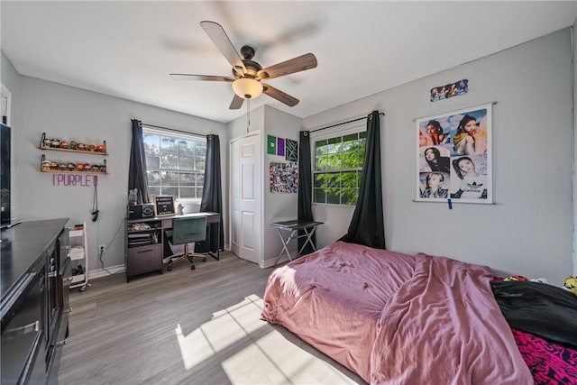 bedroom featuring light wood-type flooring, multiple windows, baseboards, and a ceiling fan