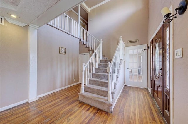 stairway with a textured ceiling, ornamental molding, a high ceiling, and hardwood / wood-style flooring