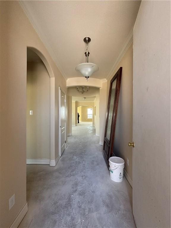 hall with ornamental molding, arched walkways, baseboards, and unfinished concrete floors