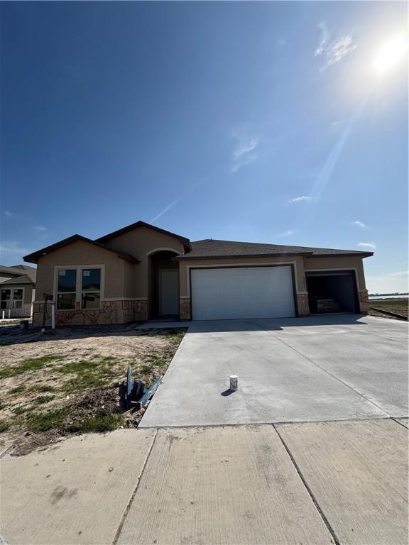 ranch-style house featuring a garage, stone siding, driveway, and stucco siding