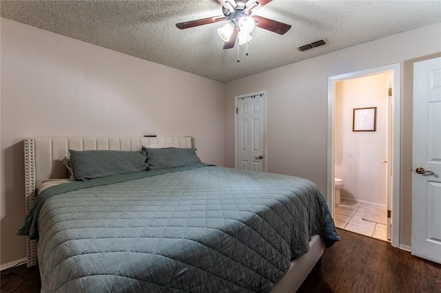 bedroom with ceiling fan, ensuite bathroom, dark wood-type flooring, and a textured ceiling