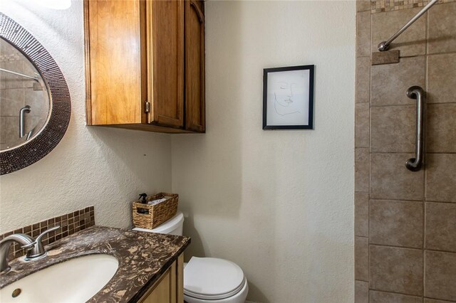 bathroom with toilet, vanity, and tiled shower