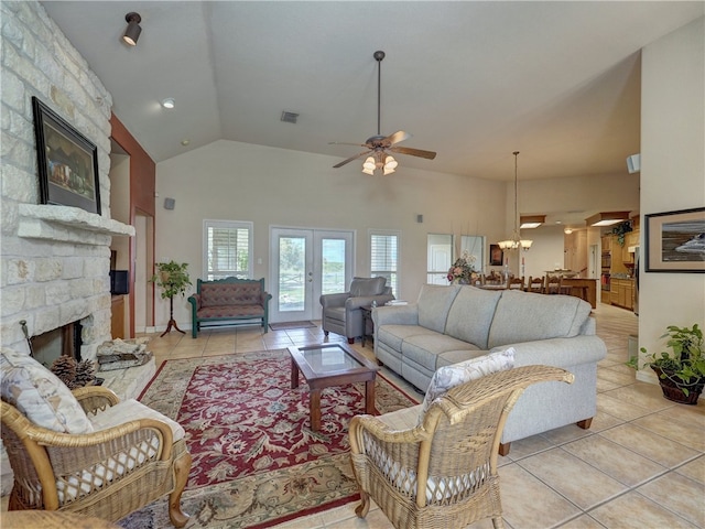 tiled living room featuring french doors, ceiling fan with notable chandelier, high vaulted ceiling, and a stone fireplace