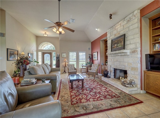 tiled living room with built in shelves, high vaulted ceiling, a stone fireplace, and ceiling fan