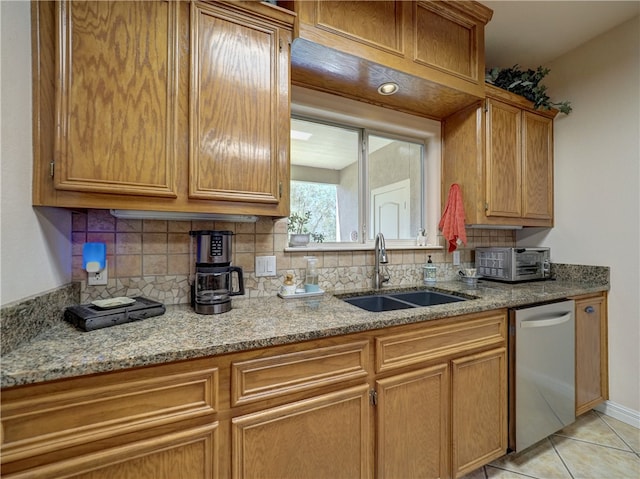 kitchen featuring tasteful backsplash, light stone counters, stainless steel dishwasher, sink, and light tile patterned floors