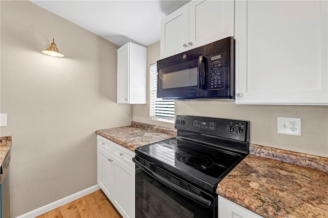 kitchen featuring light wood-type flooring, white cabinetry, dark stone counters, and black appliances