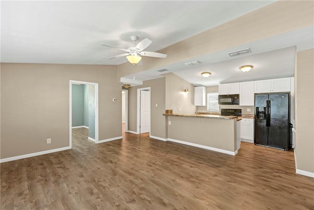 kitchen featuring hardwood / wood-style floors, black appliances, kitchen peninsula, light stone countertops, and white cabinetry