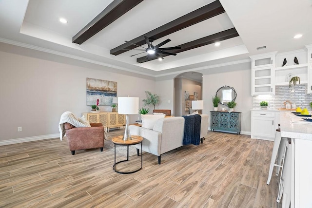 living area with arched walkways, a raised ceiling, a ceiling fan, beamed ceiling, and light wood-style floors