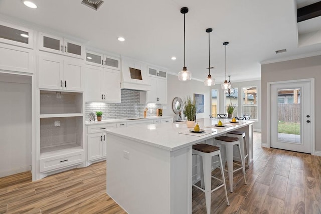 kitchen with a center island, white cabinetry, decorative backsplash, glass insert cabinets, and pendant lighting