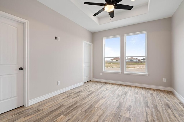 unfurnished room featuring baseboards, ceiling fan, a raised ceiling, and light wood-style floors