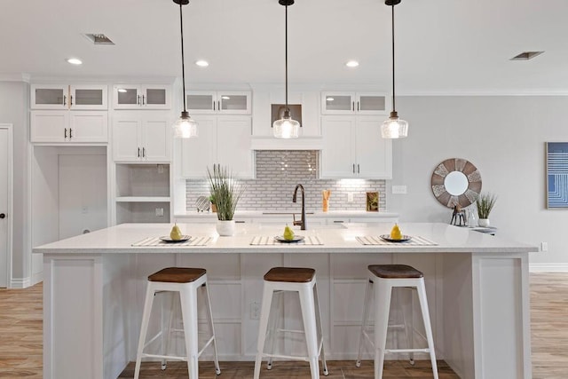 kitchen with glass insert cabinets, decorative light fixtures, a center island with sink, and white cabinetry