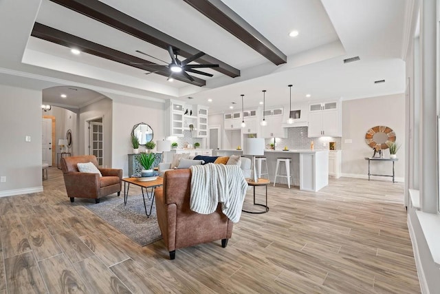 living room with arched walkways, beamed ceiling, light wood-type flooring, and a raised ceiling