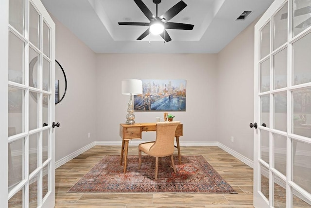 office area featuring french doors, a tray ceiling, light wood-type flooring, and baseboards