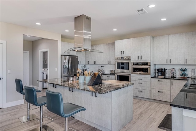 kitchen with dark stone counters, stainless steel appliances, visible vents, and island range hood