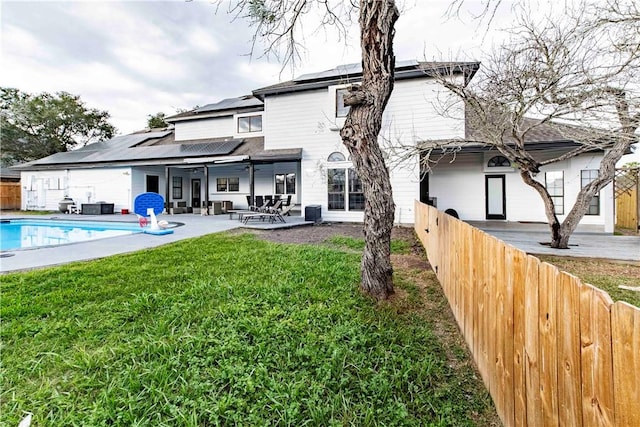 back of house featuring a fenced in pool, solar panels, a lawn, a fenced backyard, and a patio area