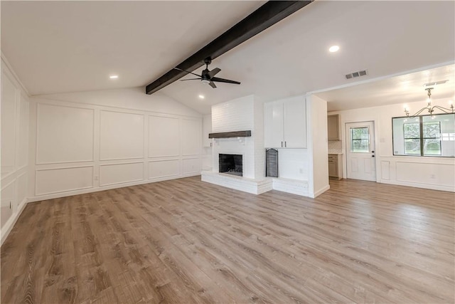 unfurnished living room featuring visible vents, lofted ceiling with beams, a fireplace, a decorative wall, and ceiling fan with notable chandelier