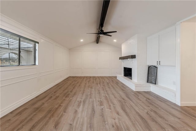 unfurnished living room with lofted ceiling with beams, a brick fireplace, light wood-style flooring, and a decorative wall