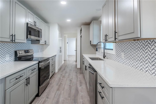 kitchen featuring decorative backsplash, light wood-style flooring, stainless steel appliances, light countertops, and a sink