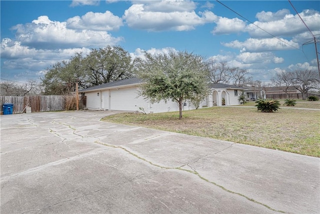 exterior space featuring concrete driveway, a lawn, an attached garage, and fence