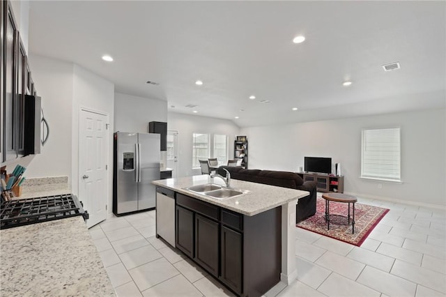 kitchen with sink, light stone counters, a center island with sink, light tile patterned floors, and stainless steel appliances