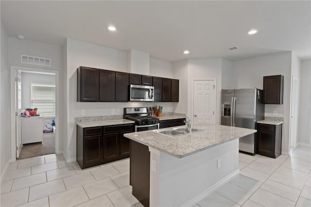 kitchen with appliances with stainless steel finishes, a kitchen island with sink, sink, and light tile patterned floors