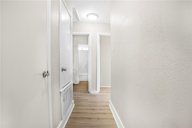 corridor featuring light wood finished floors, visible vents, baseboards, and a textured wall